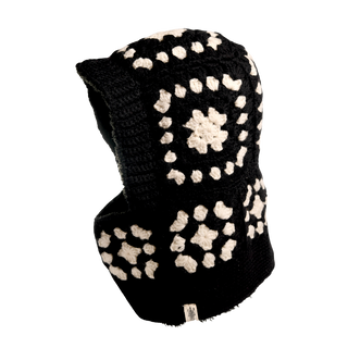 The Crochet Patch Hood, featuring a black crochet design with white geometric square and circular patterns, is depicted against a black background. There is a tag at the bottom edge of the hood.