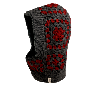 The Crochet Patch Hood, a gray and red crocheted balaclava with a striking geometric pattern, is displayed against a black background. This hood-like design covers both the head and neck while leaving an opening for the face.