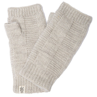A pair of Checkered Handwarmers in light beige is pictured. Handmade in Nepal from 100% wool, these knitted fingerless gloves feature a ribbed texture at the wrist and finger openings, along with a patterned knit design on the body. A small sewn-on tag with a logo is visible near the wrist end of one glove.
