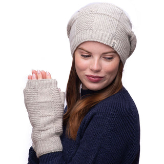 A young woman with long brown hair is wearing a gray knit beanie and matching Checkered Handwarmers made from 100% wool. She is looking down and to her right with a neutral expression, also dressed in a navy blue knit sweater against a plain white background.