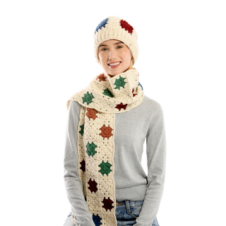 A person wearing a light grey long-sleeve shirt, a crocheted off-white beanie with colorful star patterns, and the Crochet Patch Scarf sits against a white background. The scarf also features square patches with similar star patterns in various colors.