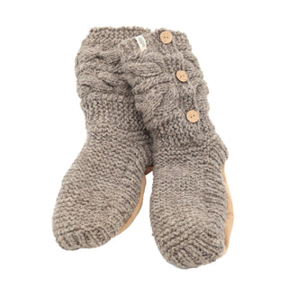 The Slipper Socks with 3 Buttons are a pair of gray knitted slipper socks showcasing a chunky knit design and accented with three wooden buttons on the side. Crafted from 100% wool, these slippers feature a soft, beige sole and are designed to provide cozy and warm comfort for winter.