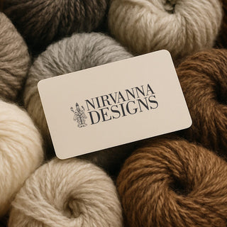 A Nirvanna Designs Gift Card rests on neutral-hued yarn skeins—an ideal gift for any creative soul.