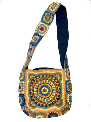 The Cotton Crochet Messenger Bag is handmade with colorful geometric squares and circles in yellow, blue, green, and orange. The wide strap features matching crocheted squares for a coordinated look.