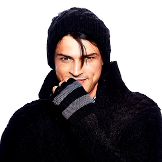 A man wearing a black sweater, Striped and Solid Fingerless Gloves, and a striped hat for a winter look.