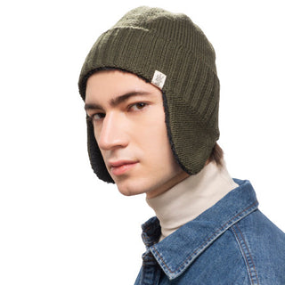 A person is wearing a Rib Band Earflap Hat featuring a green knit design and a white tag on the side. They have a neutral expression, dressed in a blue denim jacket and beige turtleneck sweater, perfect for chilly weather.