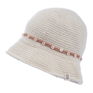 The Emily Sun Hat is a cream-colored, knitted sun hat with a textured pattern. It features a thin, brown band around it, accented with small white buttons. Handmade from 100% wool, the hat has a slightly flared brim and a small tag with the logo near the edge. The background is plain white.