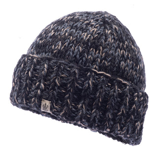 The Marbled Rib Fold Beanie is a dark blue and gray marled knit beanie with a folded brim, handmade in Nepal. It features a small rectangular label with a logo on the brim and is crafted from Merino wool, offering a thick and warm texture that is perfect for cold weather.